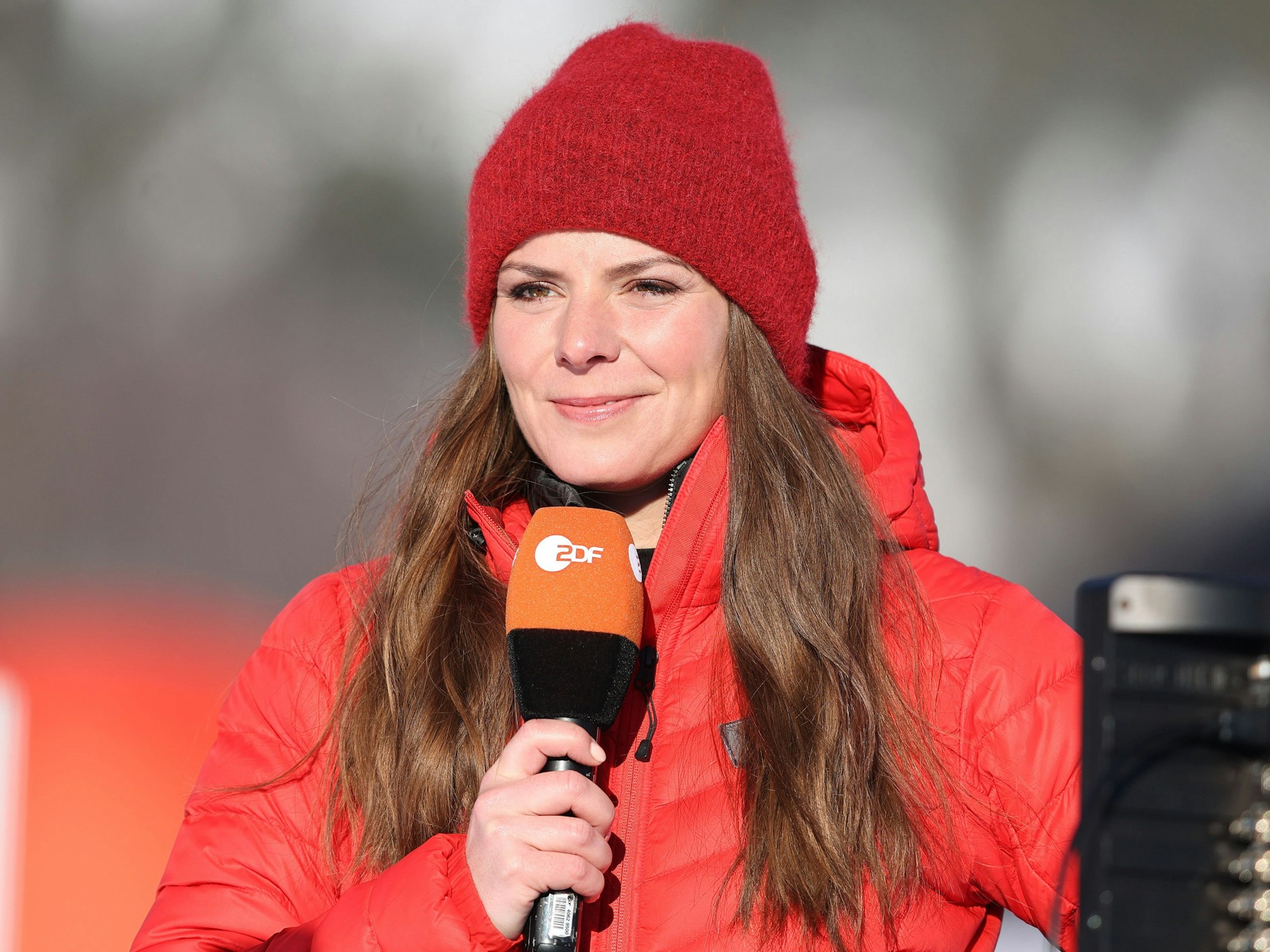 ZDF-Moderatorin Amelie Stiefvatter mit Mikro, roter Winterjacke und roter Wollmütze.