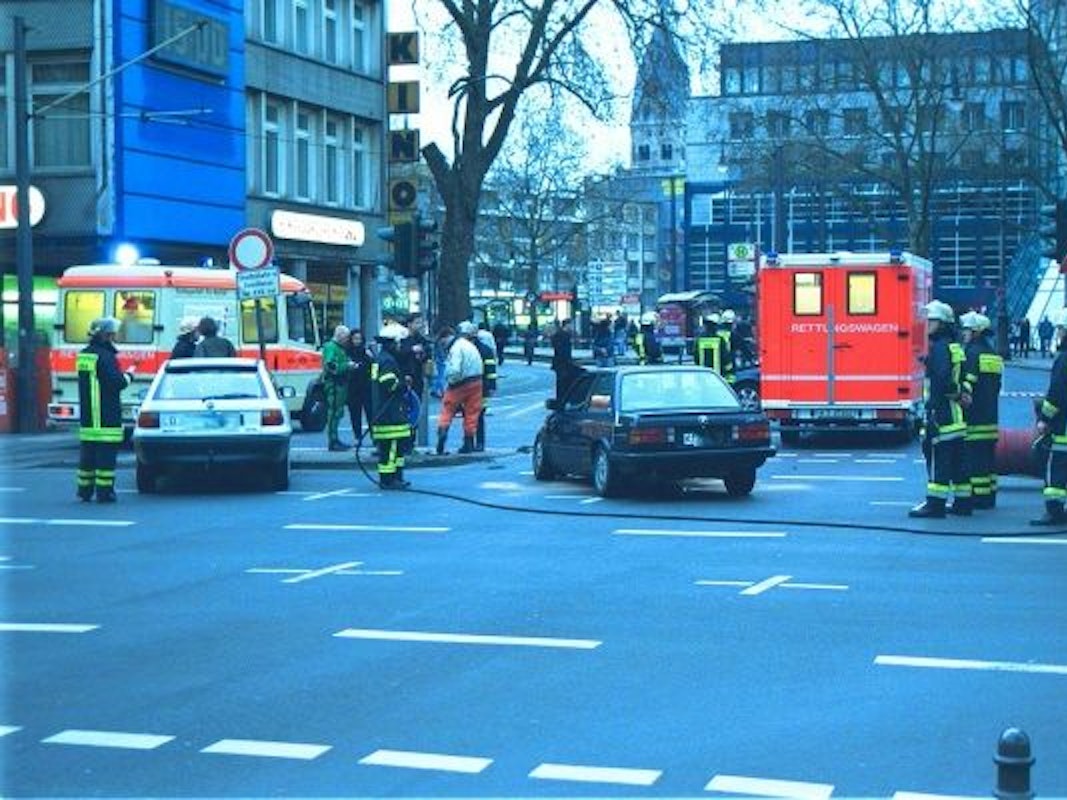 Zwei verunglückte Autos stehen auf einer Straße, um sie herum Einsatzkräfte sowie Fahrzeuge von Rettungsdienst und Feuerwehr.