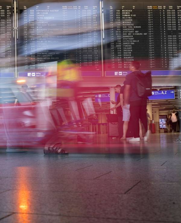 Passagiere gehen vor der Anzeigetafel im Flughafen entlang