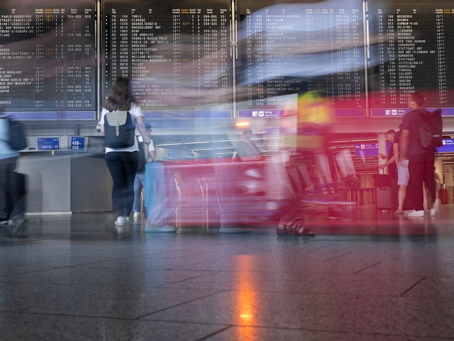 Passagiere gehen vor der Anzeigetafel im Flughafen entlang