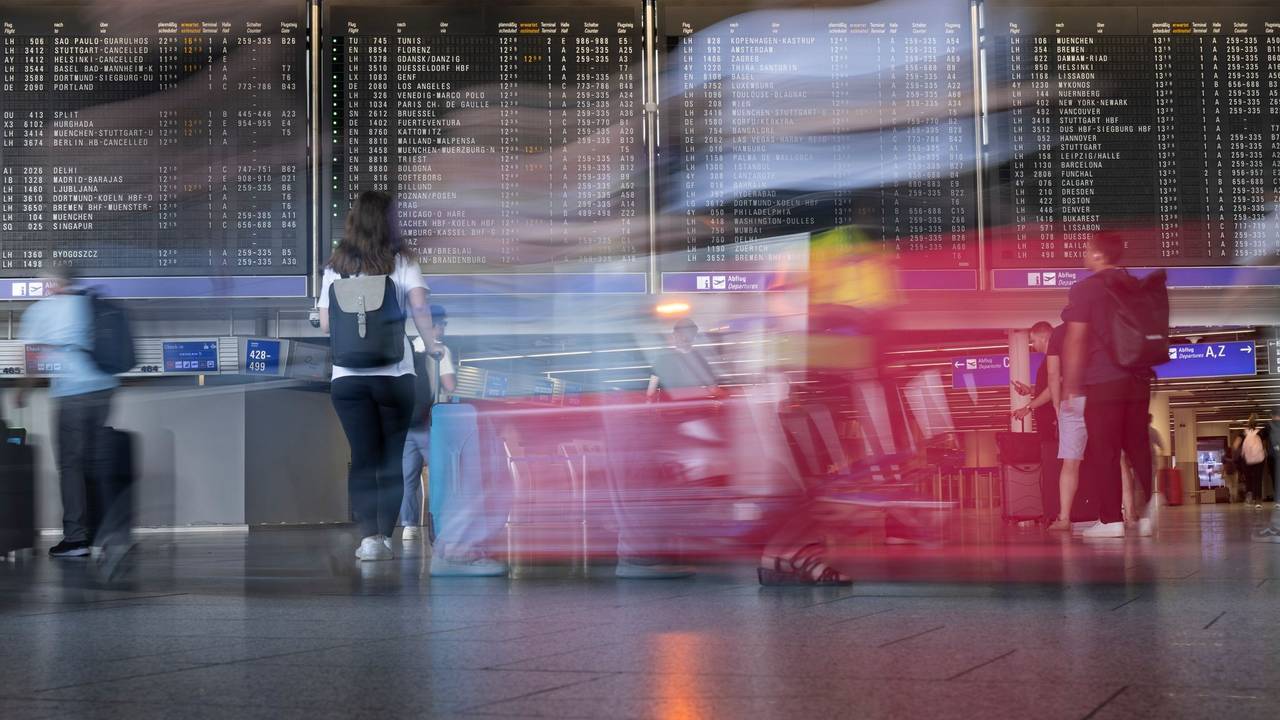 Passagiere gehen vor der Anzeigetafel im Flughafen entlang