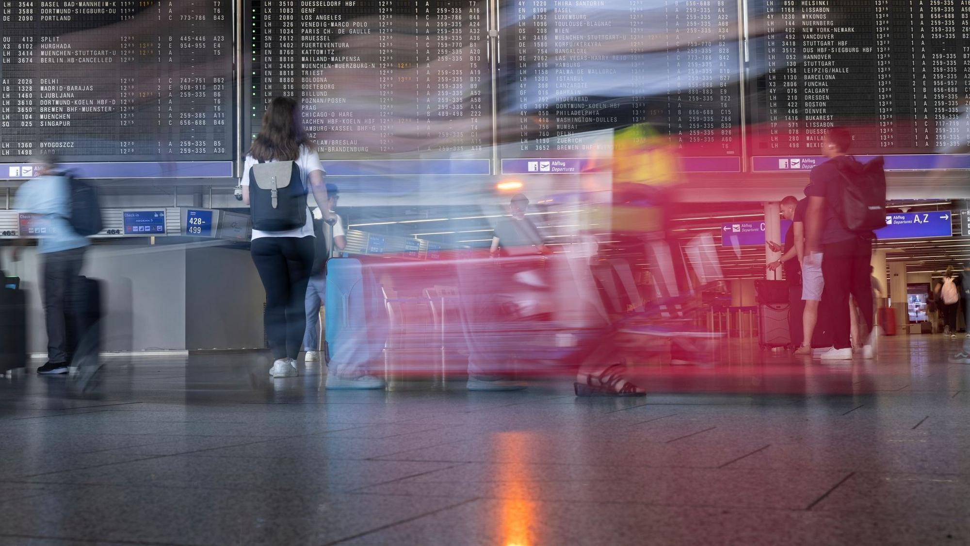 Passagiere gehen vor der Anzeigetafel im Flughafen entlang