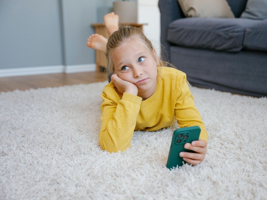 Mädchen mit Smartphone auf Teppich