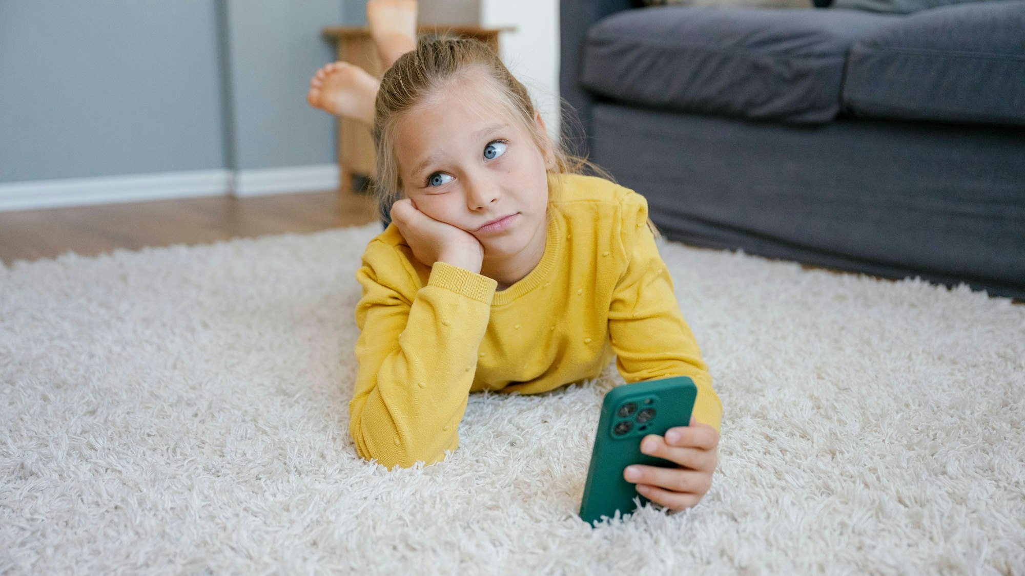 Mädchen mit Smartphone auf Teppich