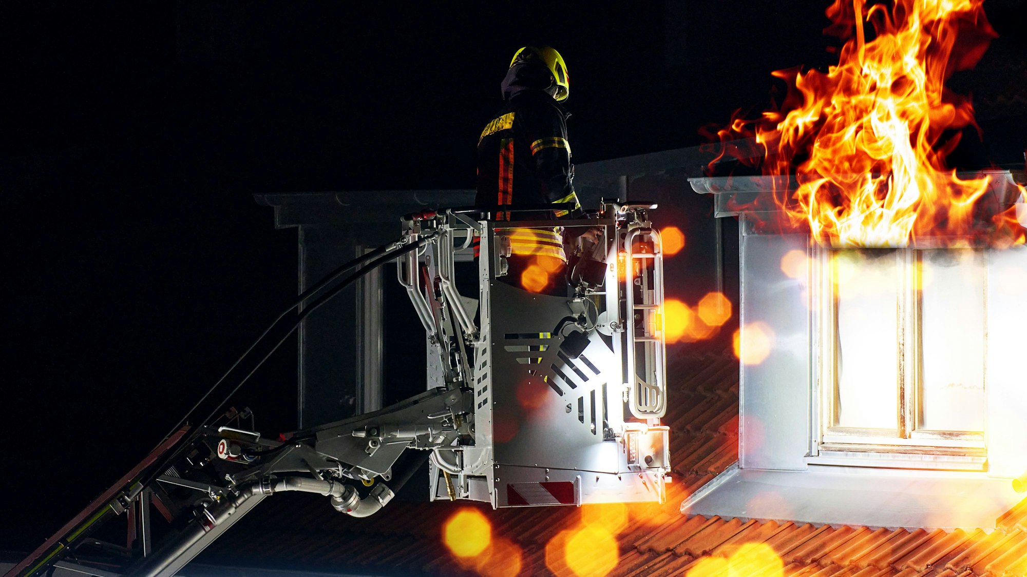 Das Symbolfoto zeigt einen Feuerwehrmann bei einem Dachstuhlbrand auf einer Drehleiter.