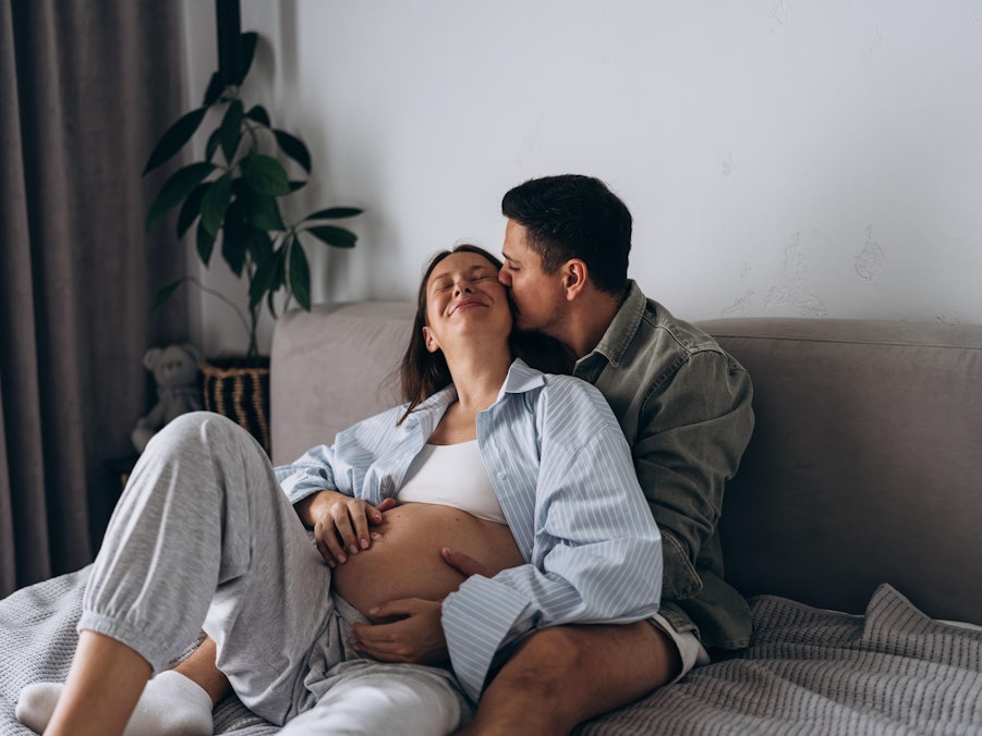 Eine schwangere Frau liegt mit ihrem Partner kuschelnd im Bett