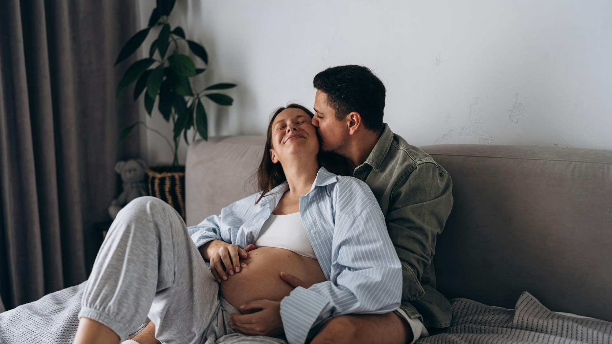 Eine schwangere Frau liegt mit ihrem Partner kuschelnd im Bett