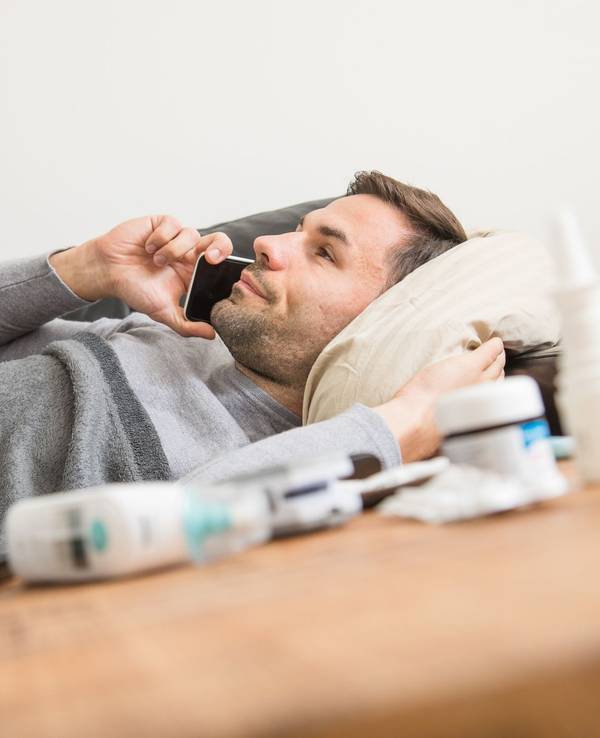 Ein Mann liegt krank auf einem Sofa und telefoniert