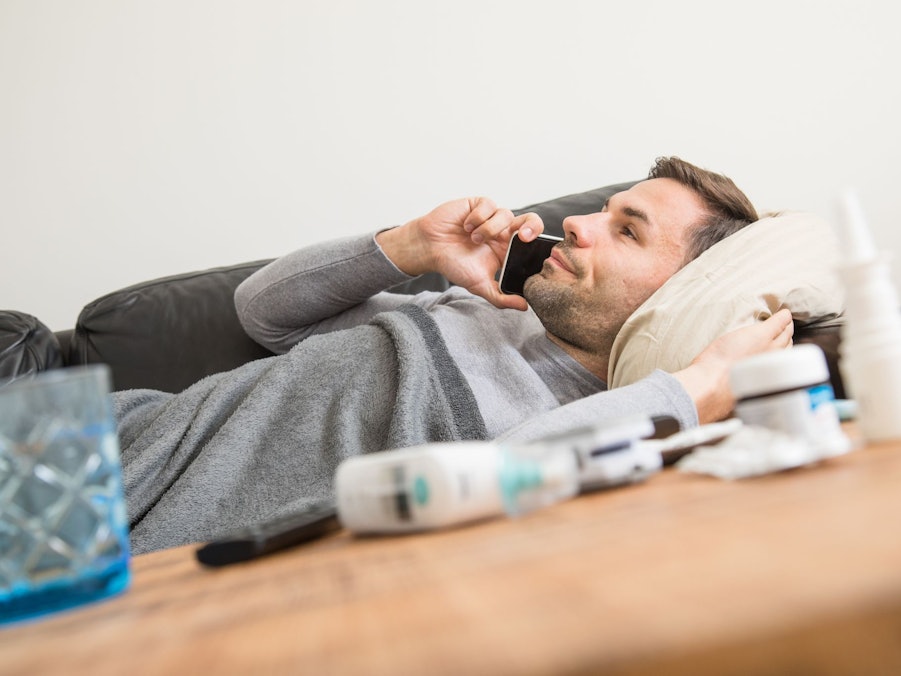 Ein Mann liegt krank auf einem Sofa und telefoniert