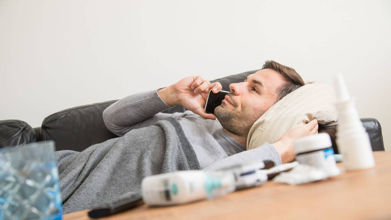 Ein Mann liegt krank auf einem Sofa und telefoniert