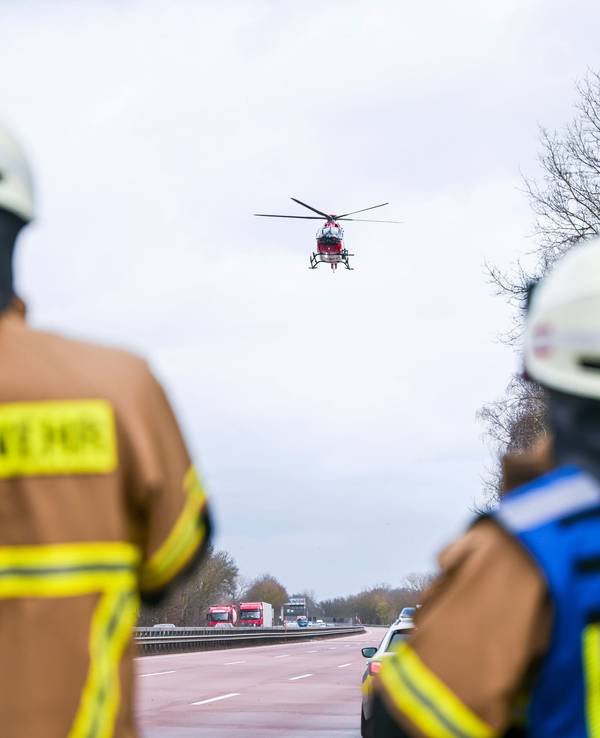 Feuerwehrleute beobachten einen Rettungshubschrauber, der auf der Autobahn landet.