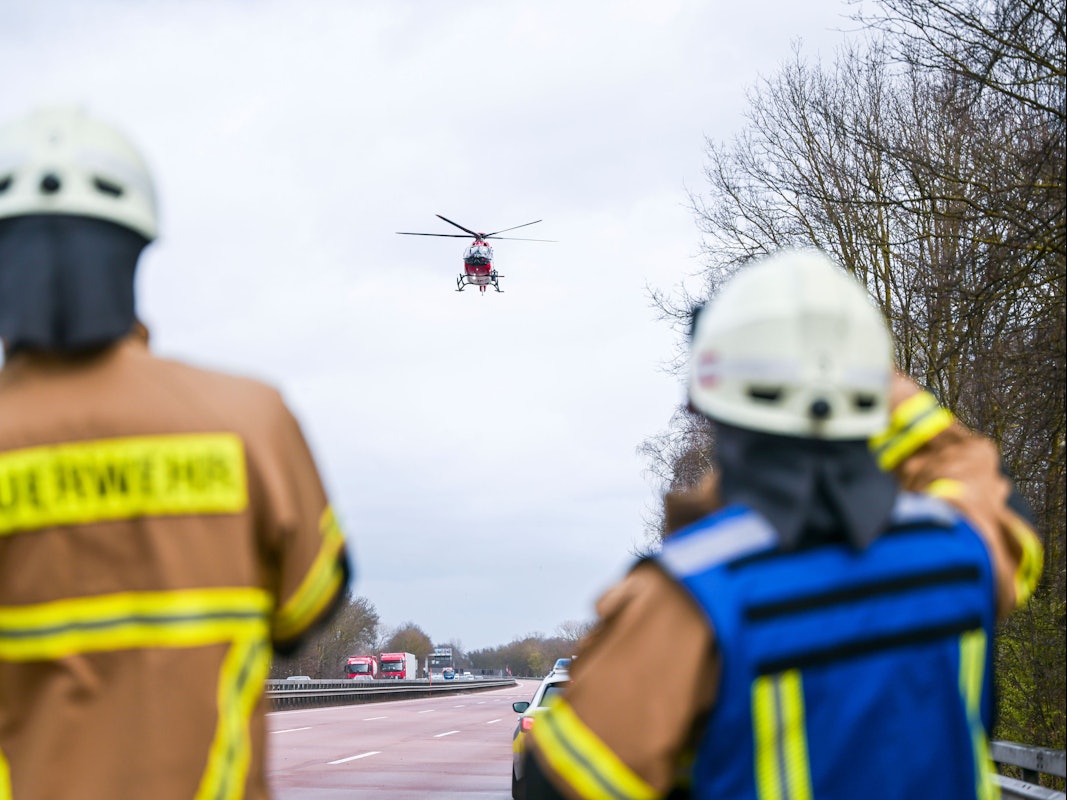 Feuerwehrleute beobachten einen Rettungshubschrauber, der auf der Autobahn landet.