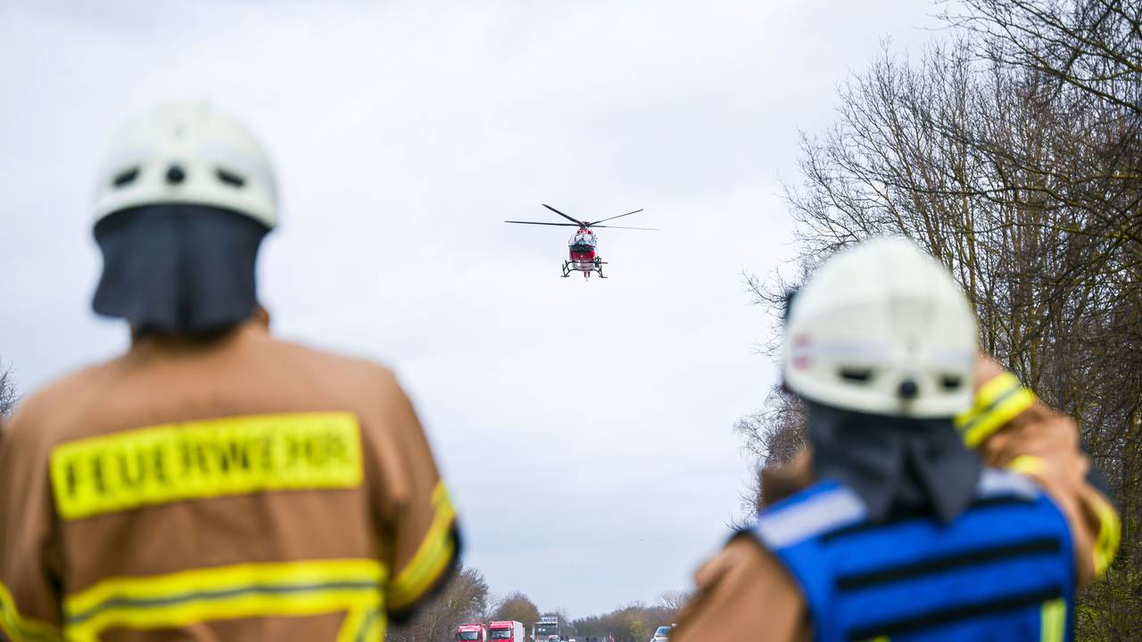 Feuerwehrleute beobachten einen Rettungshubschrauber, der auf der Autobahn landet.