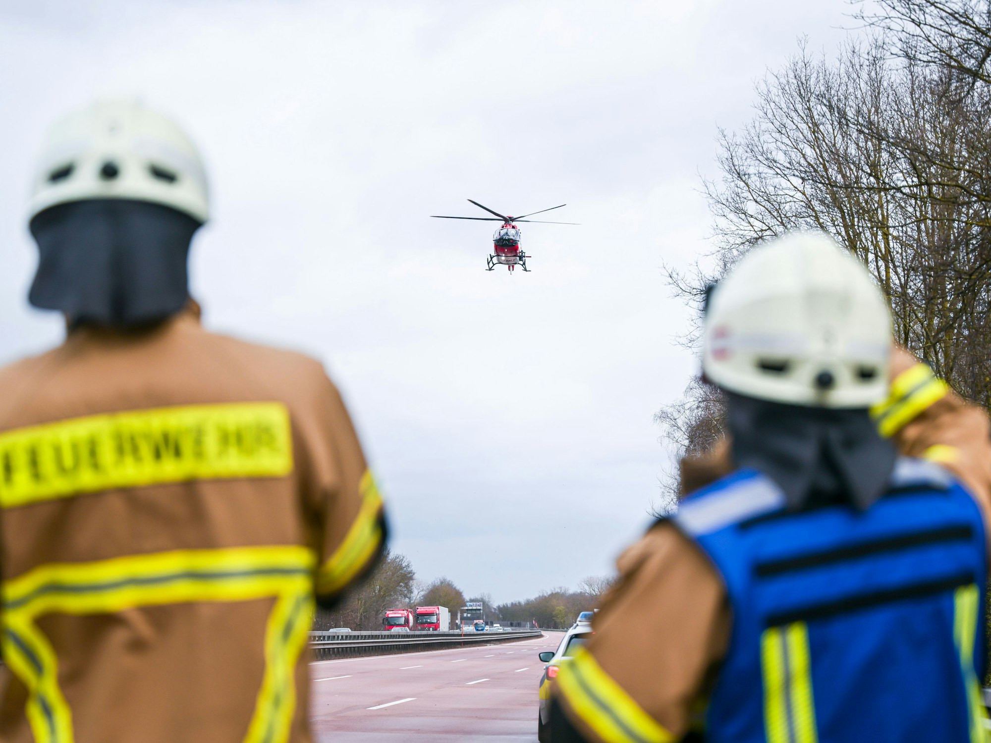 Feuerwehrleute beobachten einen Rettungshubschrauber, der auf der Autobahn landet.