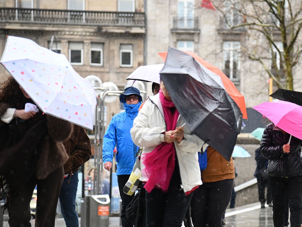 Menschen kämpfen bei stürmischem Wetter mit ihren Regenschirmen.