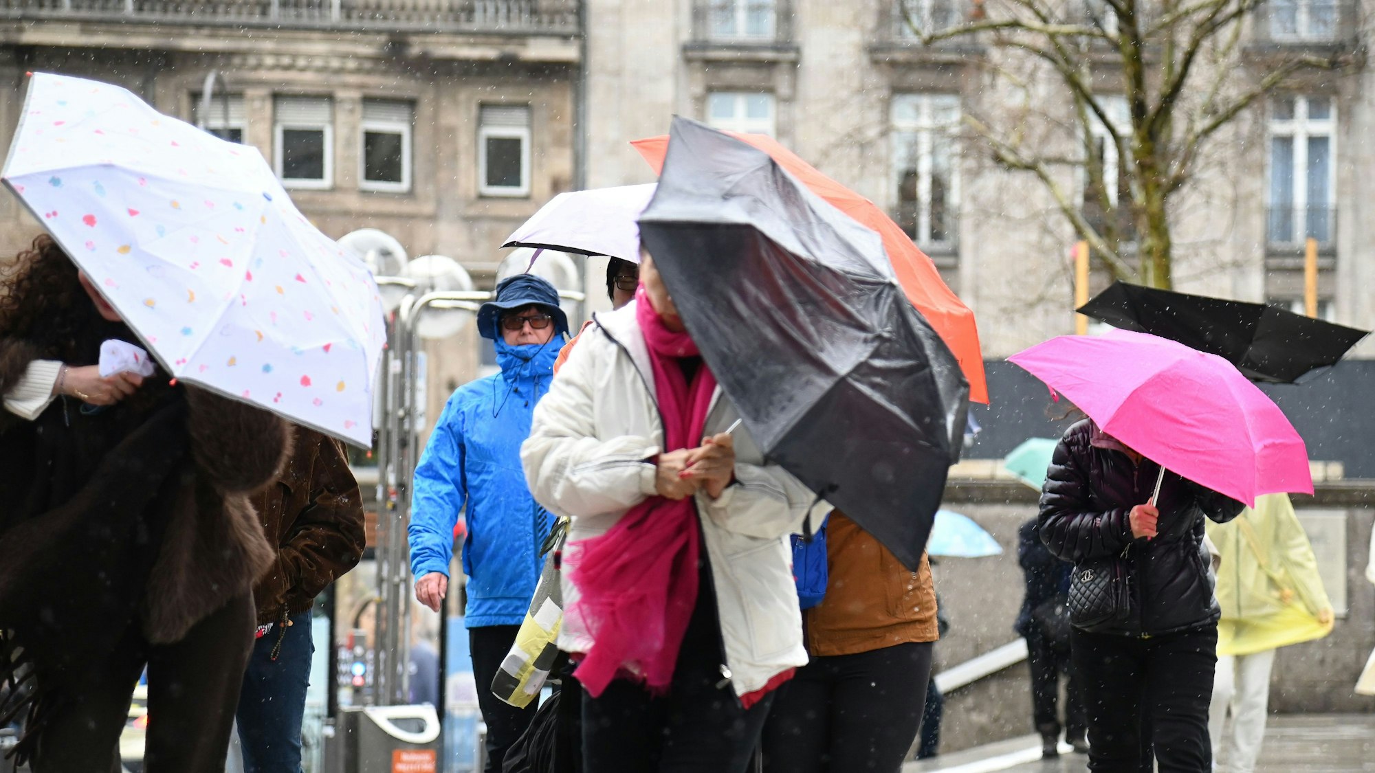 Menschen kämpfen bei stürmischem Wetter mit ihren Regenschirmen.