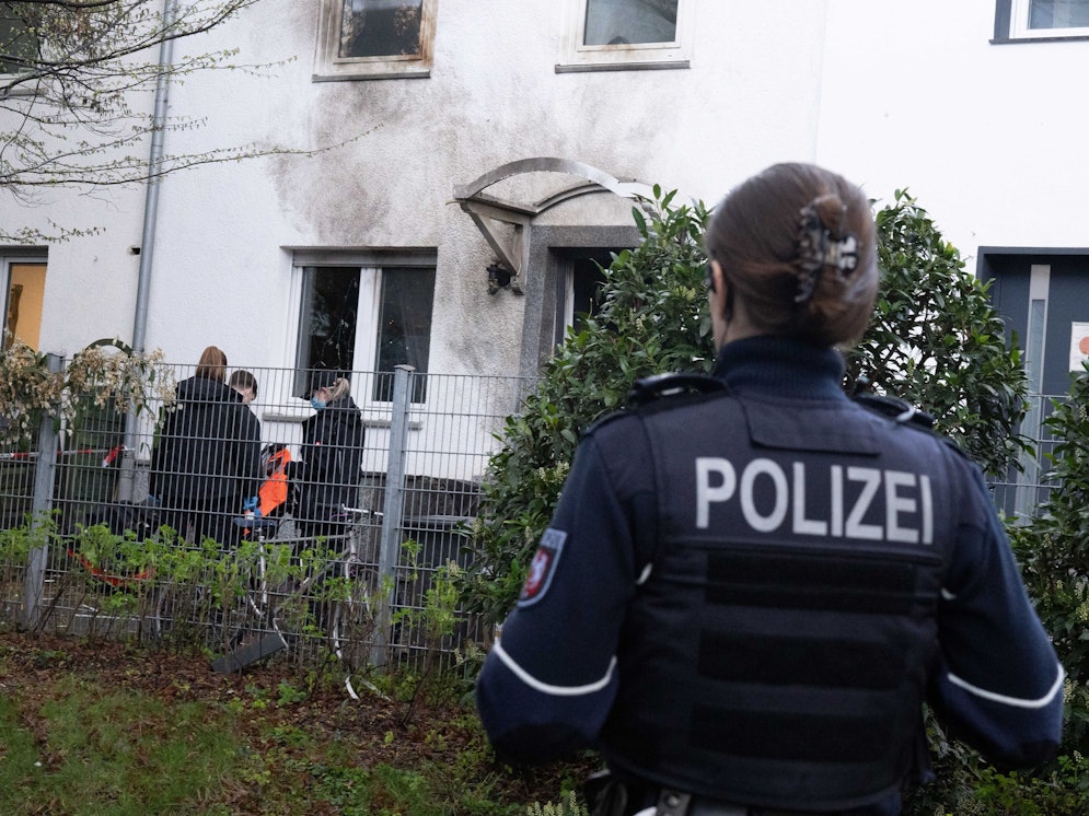 Eine Polizistin steht vor einem Haus, dessen Fassade durch die Explosion Ruß geschwärzt ist.