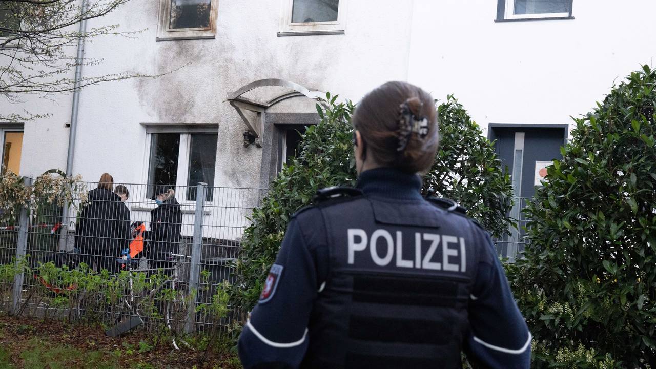 Eine Polizistin steht vor einem Haus, dessen Fassade durch die Explosion Ruß geschwärzt ist.