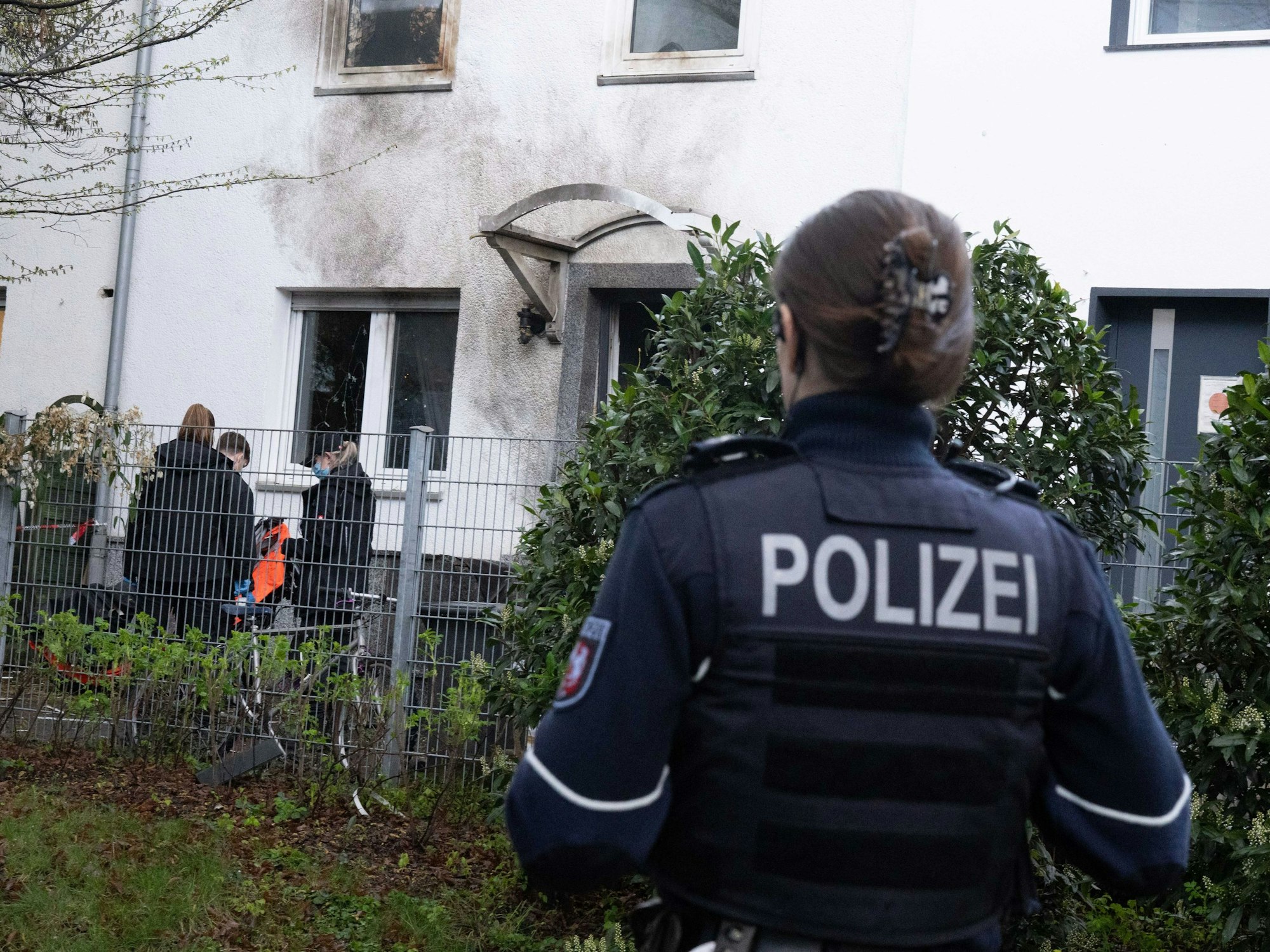 Eine Polizistin steht vor einem Haus, dessen Fassade durch die Explosion Ruß geschwärzt ist.