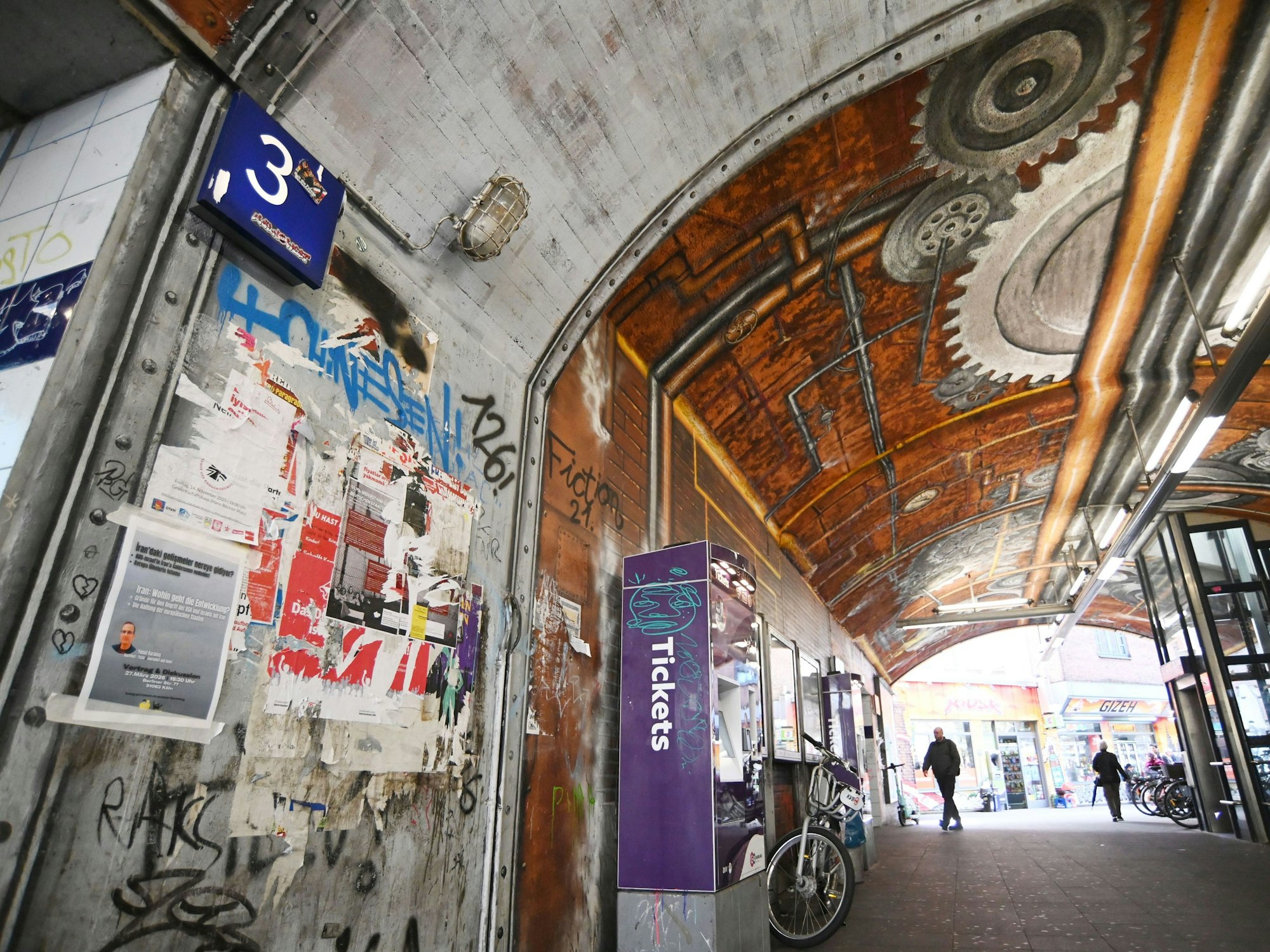 Ein Bahntunnel ist beschmiert und beklebt, auch ein dort stehender Ticketautomat ist mit Graffiti besprüht.