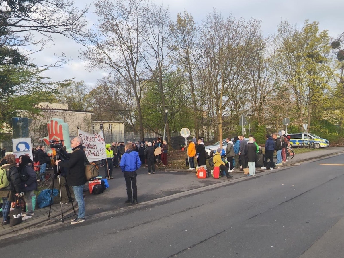Mehrere Menschen stehen mit Protestplakaten vor einem Gebäude.