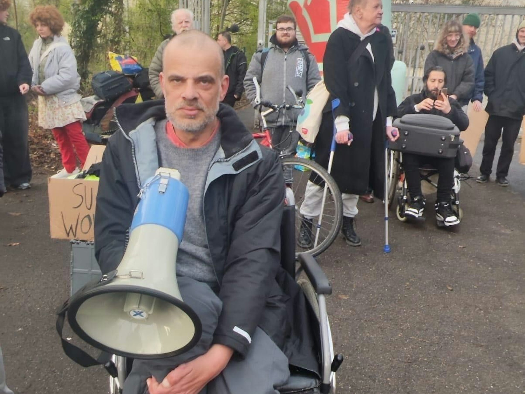 Ein Mann im Rollstuhl hält ein Megafon, hinter ihm sind weitere Personen im Rollstuhl oder auf Krücken.