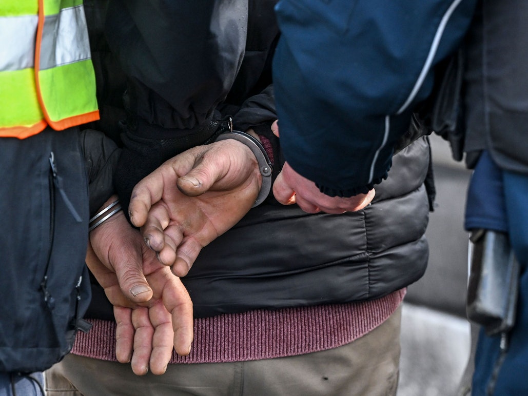Polizisten legen einem Mann Handschellen an