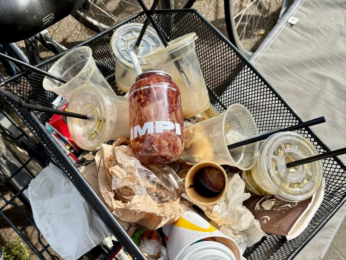 Ein Fahrradkorb ist voll mit leeren Getränkebechern aus Plastik.