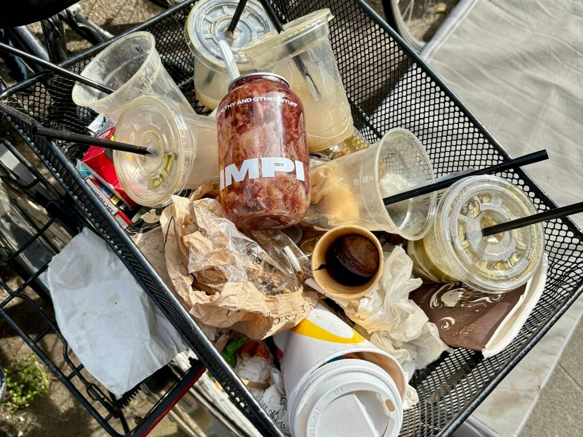 Ein Fahrradkorb ist voll mit leeren Getränkebechern aus Plastik.