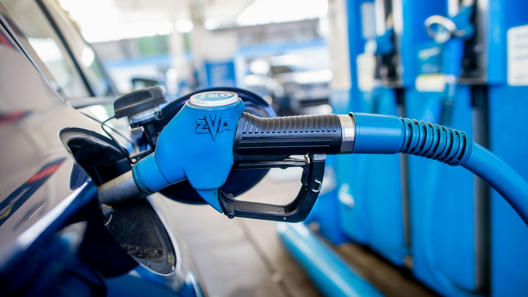 Eine Zapfpistole mit der Aufschrift „Super 95“ steckt an einer Tankstelle in der Tanköffnung eines Fahrzeugs.