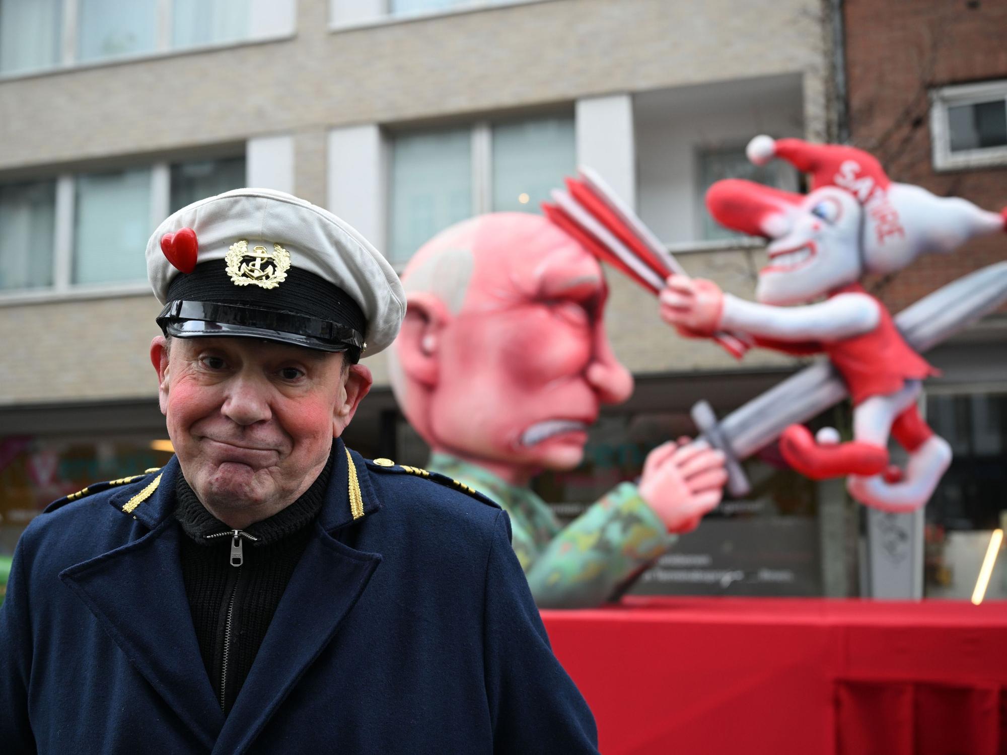 Jacques Tilly steht vor dem Mottowagen auf dem Putin die Düsseldorfer Karnevalsfigur Hoppeditz aufspießt.