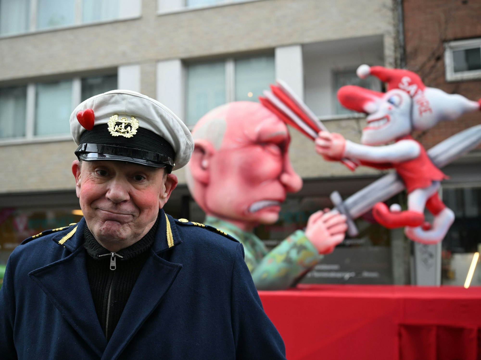 Jacques Tilly steht vor dem Mottowagen auf dem Putin die Düsseldorfer Karnevalsfigur Hoppeditz aufspießt.