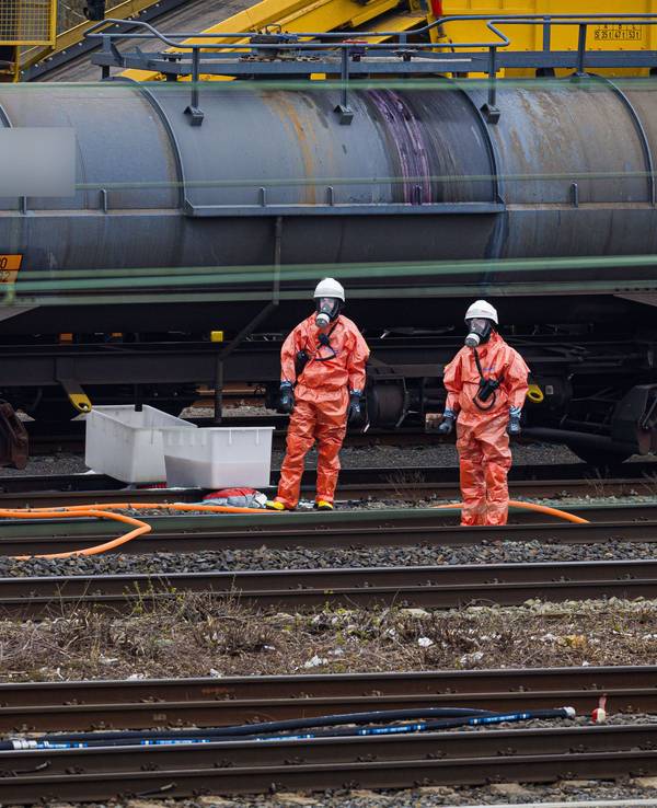 Einsatzkräfte der Feuerwehr stehen vor einem Kesselwagen am Bahnhof.