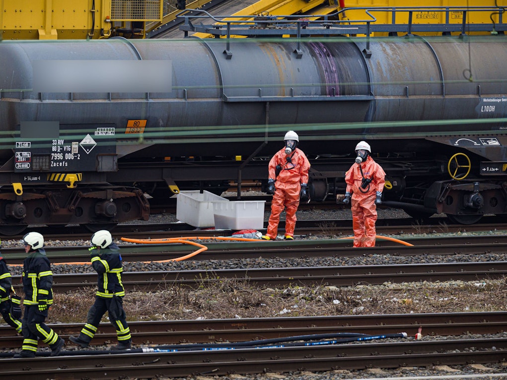 Einsatzkräfte der Feuerwehr stehen vor einem Kesselwagen am Bahnhof.