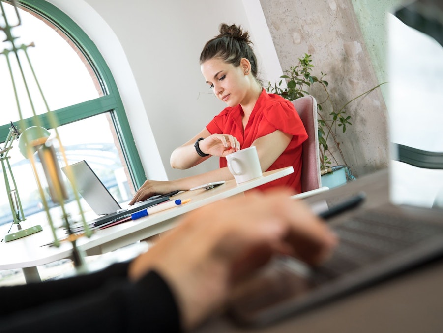 Frau schaut an ihrem Arbeitsplatz auf die Uhr