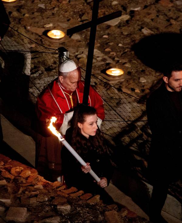 Der Papst trägt ein Holzkreuz und wird von Fackelträgern begleitet.