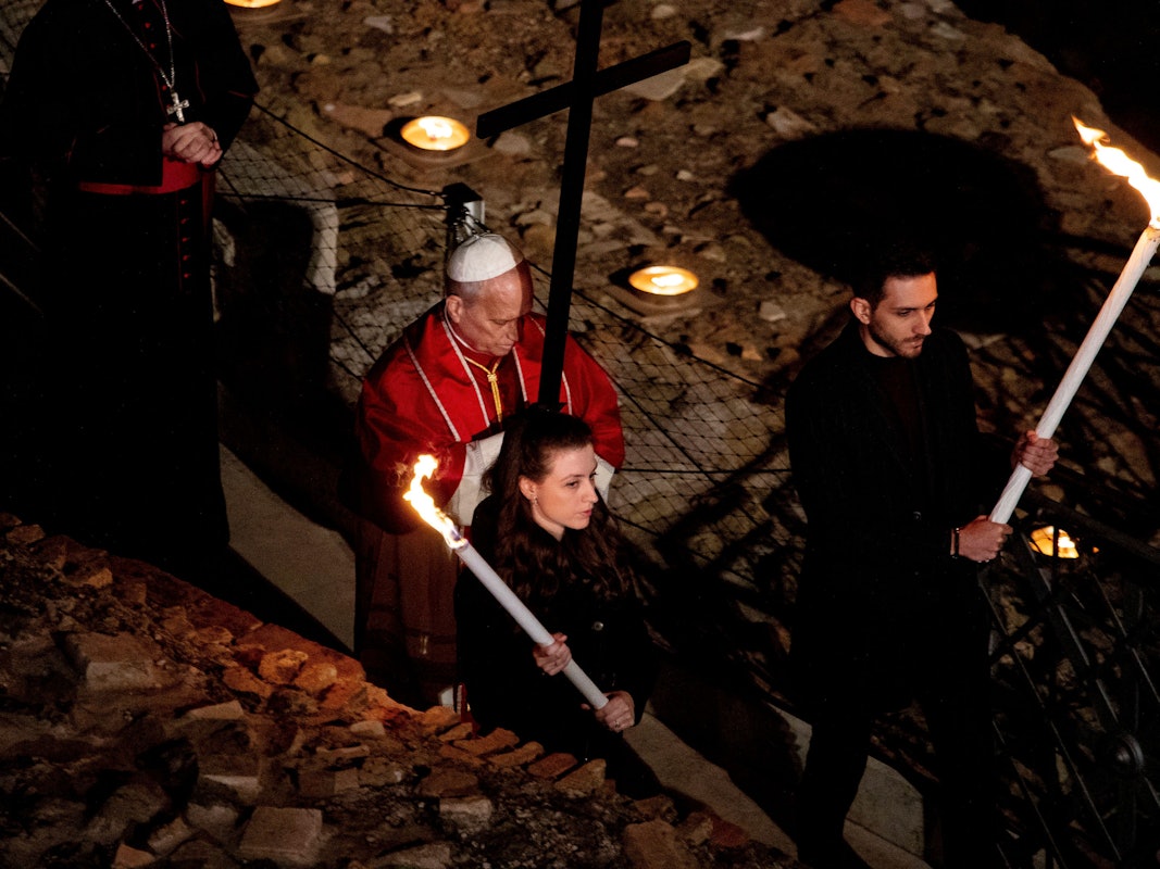 Der Papst trägt ein Holzkreuz und wird von Fackelträgern begleitet.