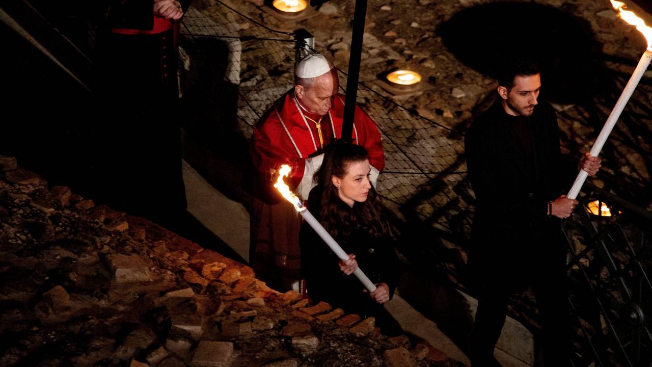 Der Papst trägt ein Holzkreuz und wird von Fackelträgern begleitet.