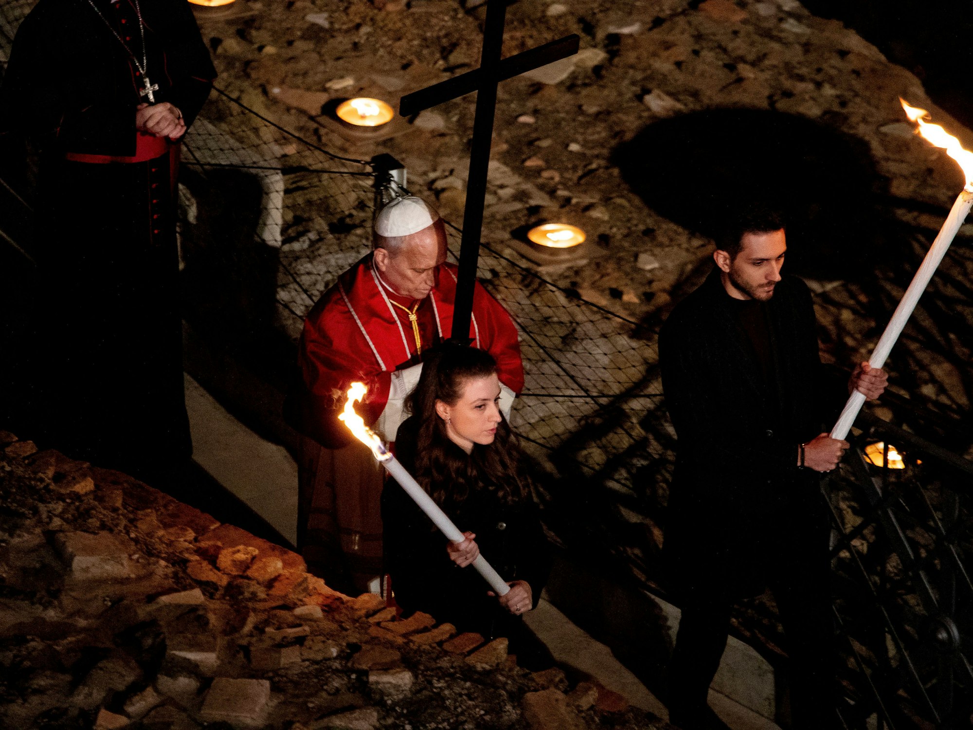 Der Papst trägt ein Holzkreuz und wird von Fackelträgern begleitet.