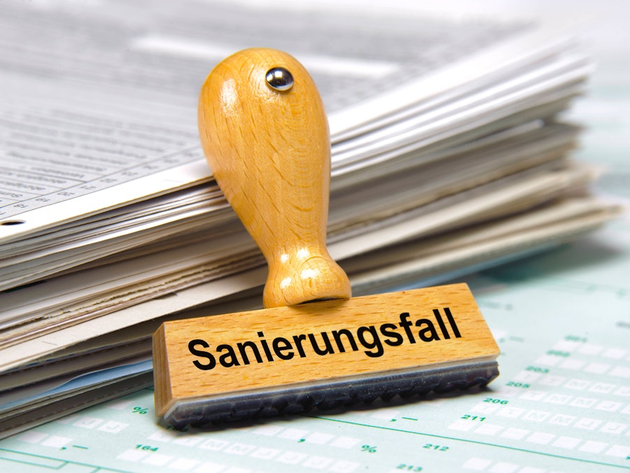 Holzstempel mit Aufschrift „Sanierungsfall“ und Papierstapel