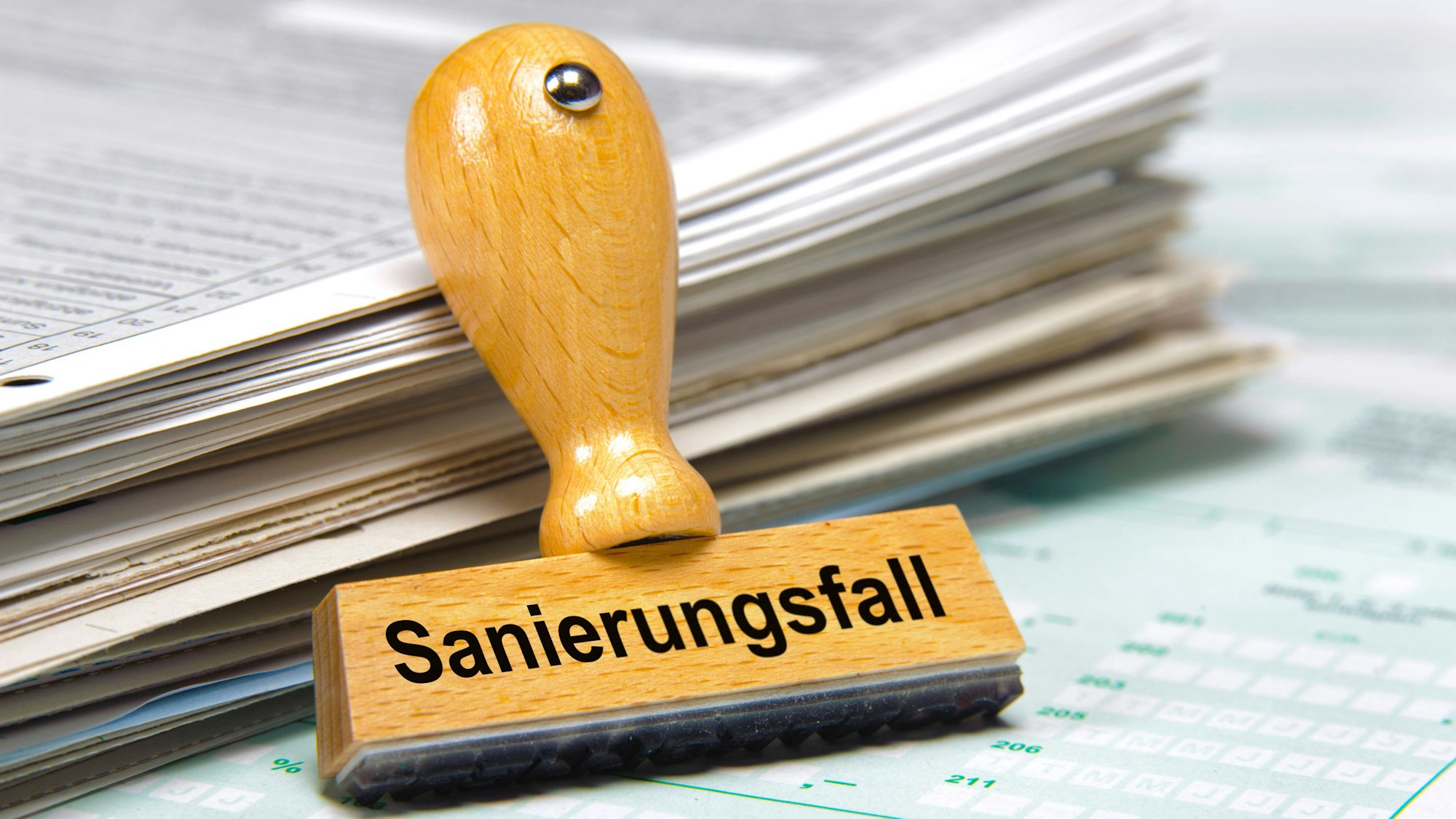 Holzstempel mit Aufschrift „Sanierungsfall“ und Papierstapel