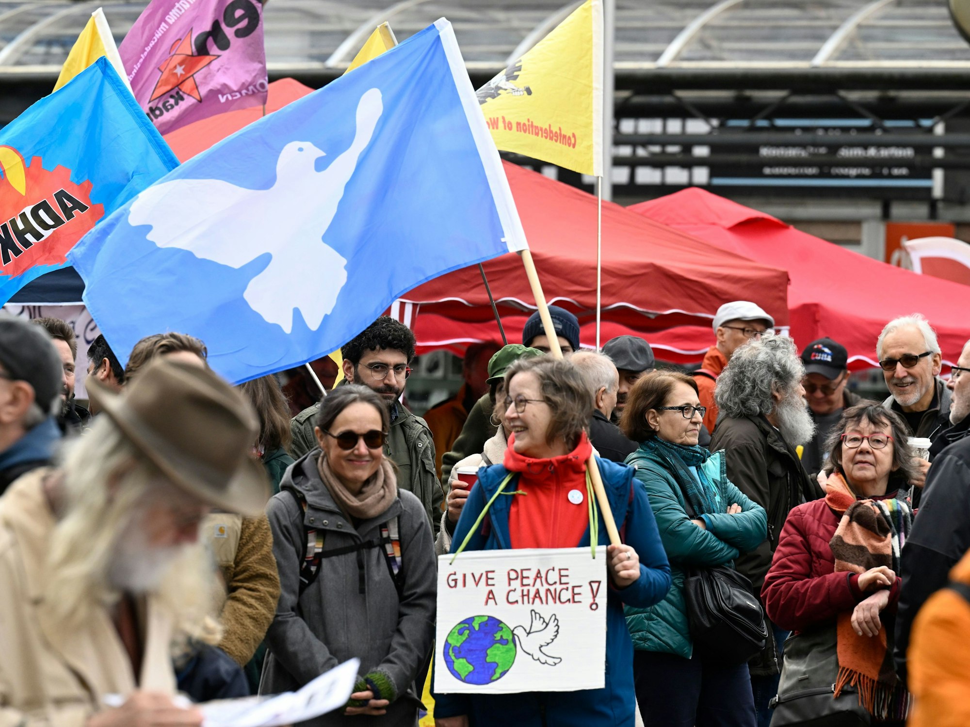Teilnehmende stehen am Start des traditionellen Ostermarschs Rhein-Ruhr mit einer Friedenstaubenfahne.