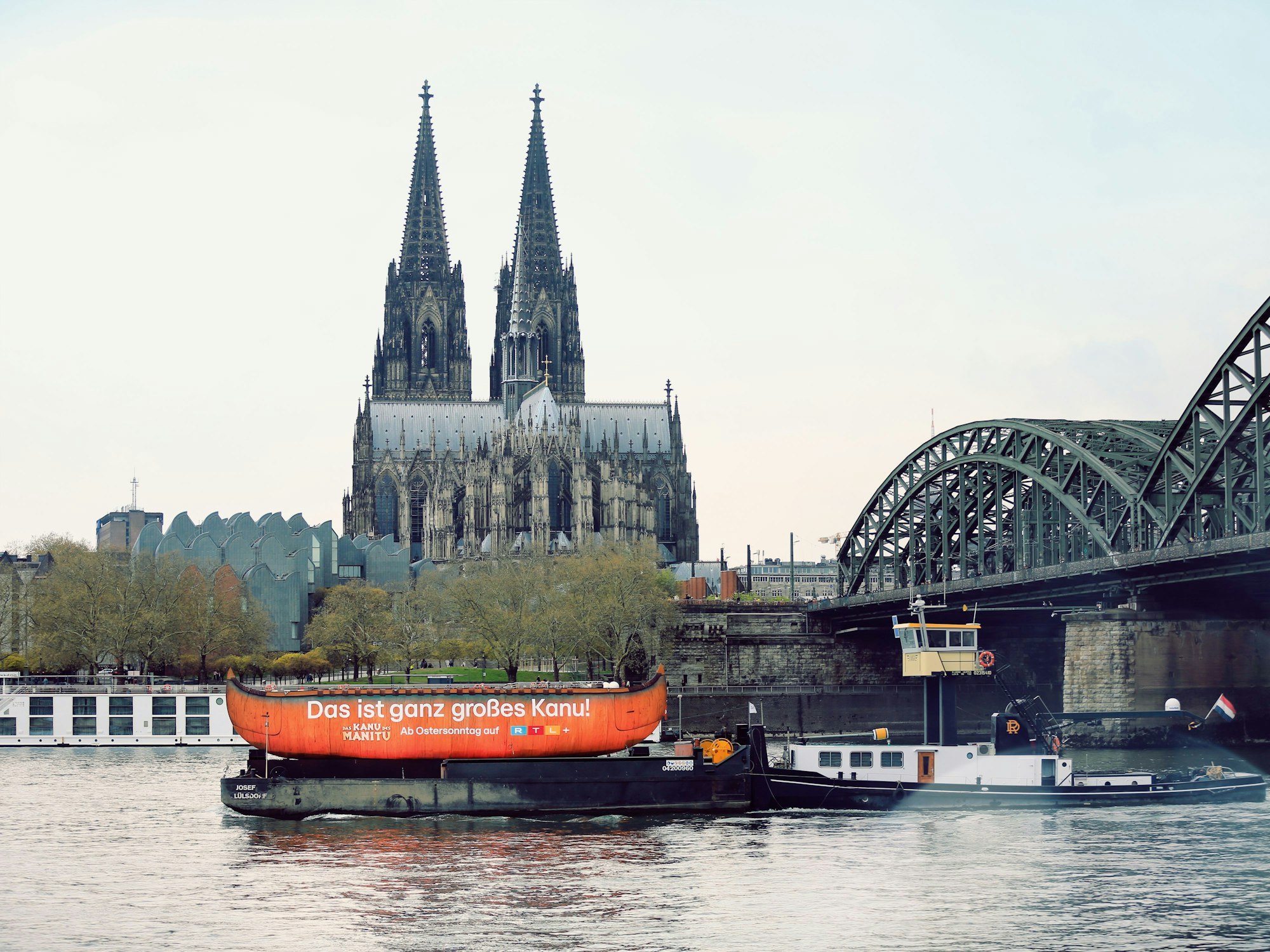Auf einem Schlepper wird das Kanu den Rhein auf- und abwärts gezogen. Darauf zu sehen der Schriftzug: Das ist ganz großes Kanu.