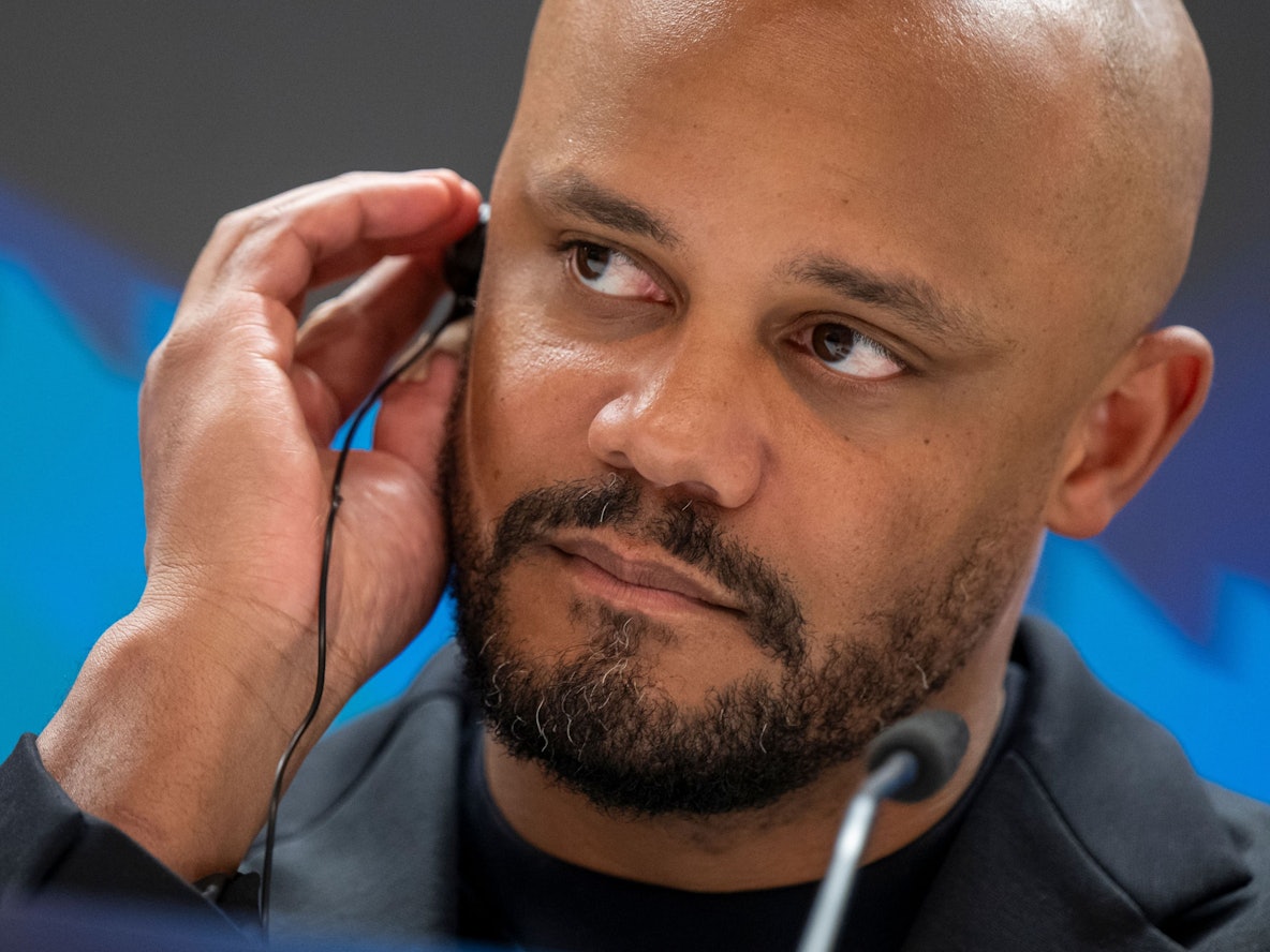 Trainer Vincent Kompany trägt bei einer Pressekonferenz einen Kopfhörer im Ohr.