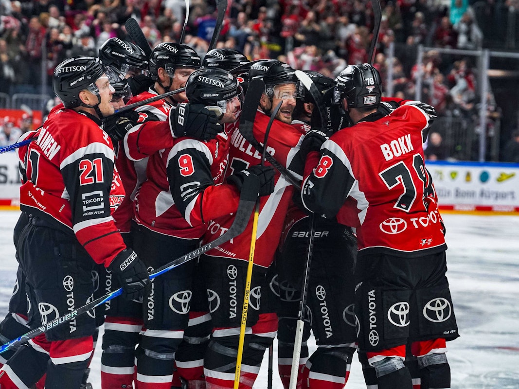 Die Spieler der Kölner Haie jubeln und umarmen sich auf dem Eis.