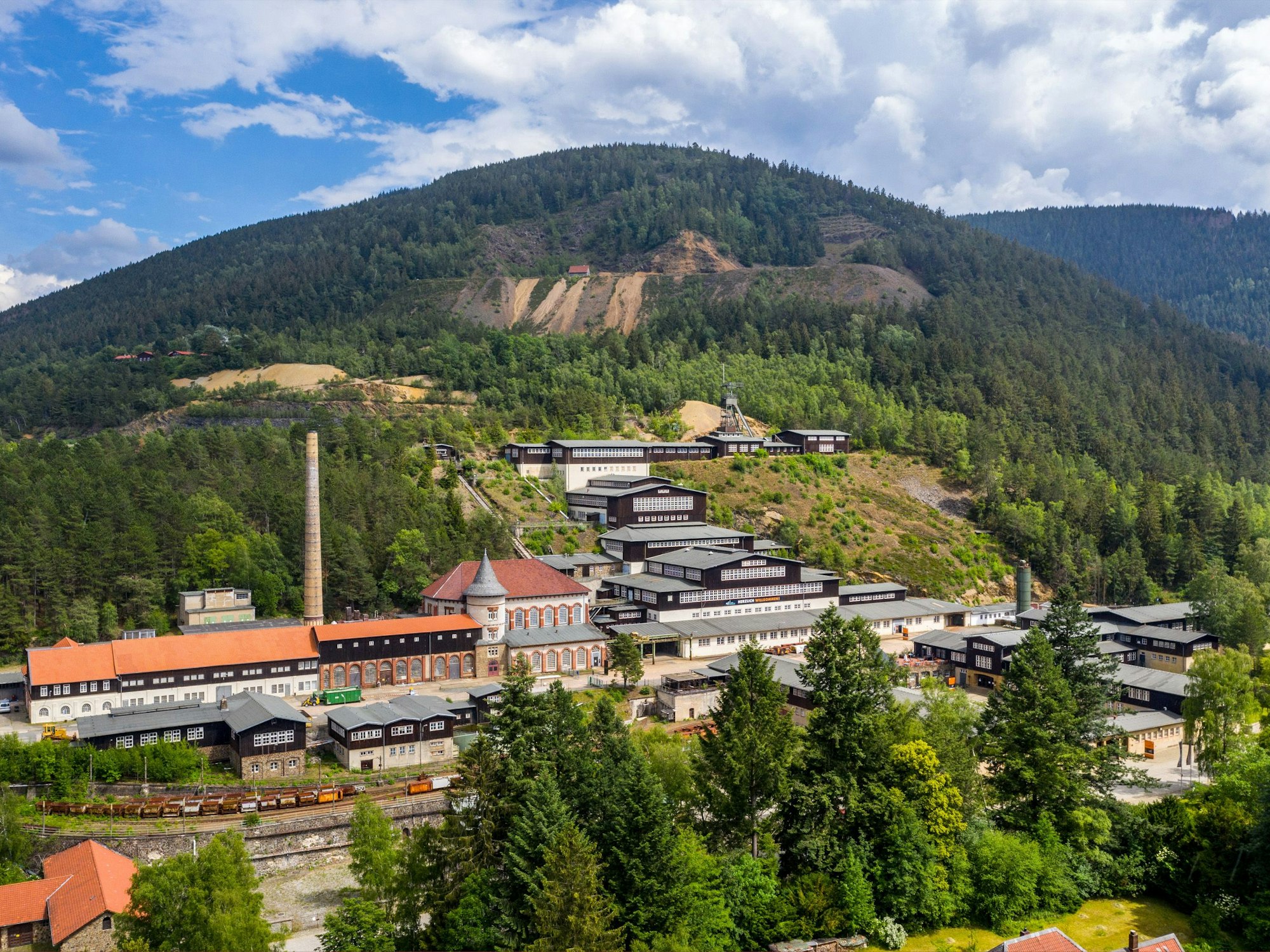 Blick auf einen grünen Hügel, vor dem Industriegebäude und andere Bauten stehen