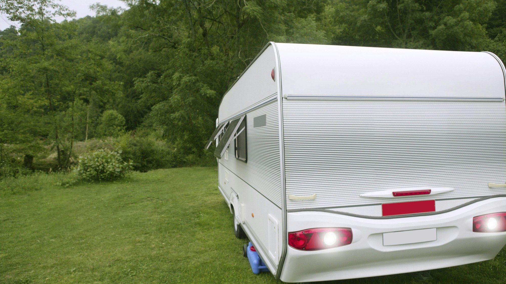 Wohnwagen auf grüner Wiese vor Wald