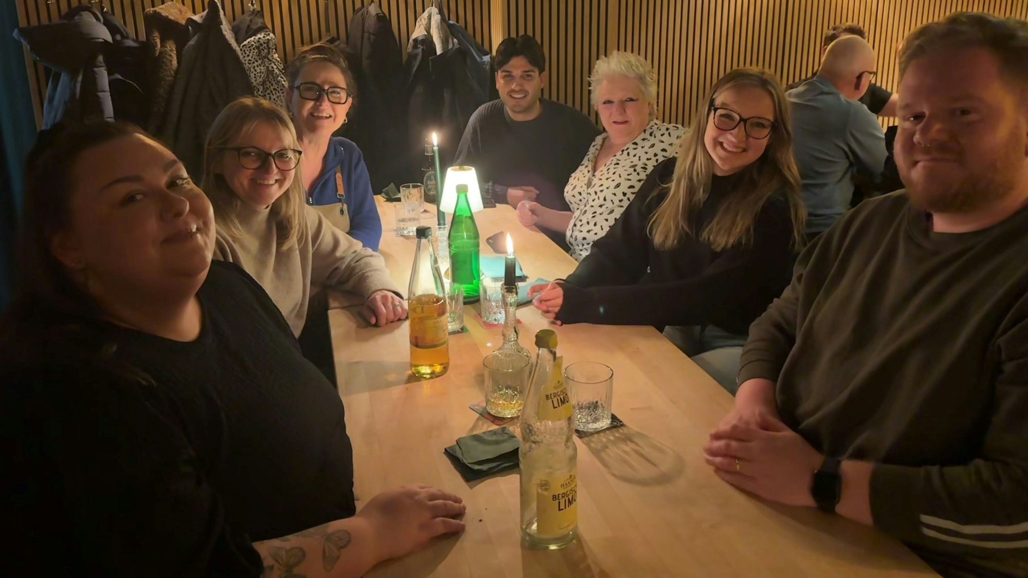 Eine Gruppe Menschen verschiedenen Alters sitzt um einen Tisch in einem Restaurant. Alle schauen fröhlich drein.