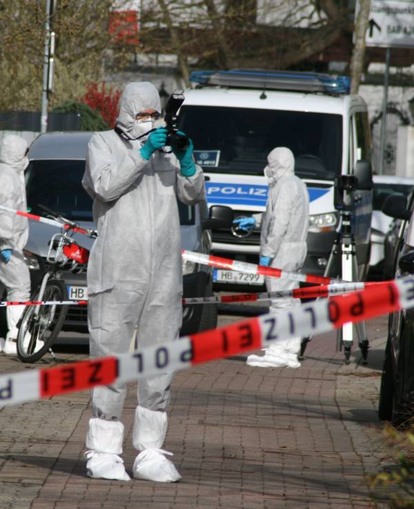 Vier Personen ind Schutzanzügen sind an dem Tatort, der mit Polizeiflatterband abgesperrt ist.