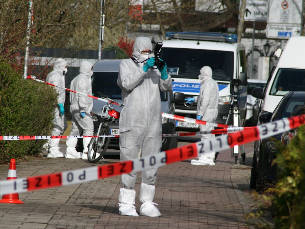 Vier Personen ind Schutzanzügen sind an dem Tatort, der mit Polizeiflatterband abgesperrt ist.